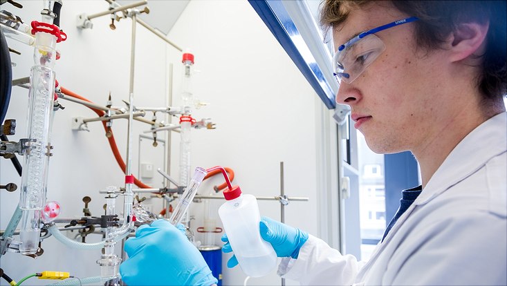 Ein junger Mann führt ein Experiment im Chemie-Labor durch. Er füllt eine Flüssigkeit in ein Reagenzglas.