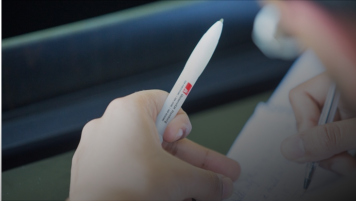 Student hält Stift mit Logo der Universität Hamburg