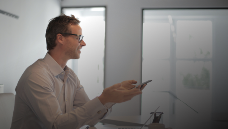 Mann mit Mobiltelefon vor Laptop