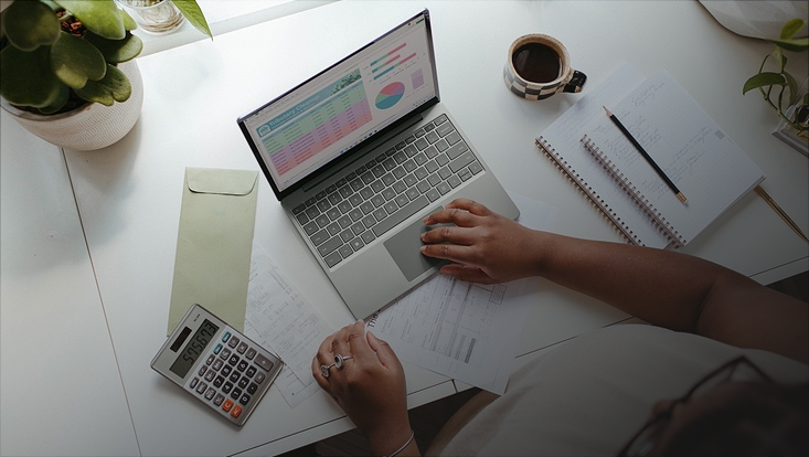 Laptop, Taschenrechner und Papiere auf Schreibtisch