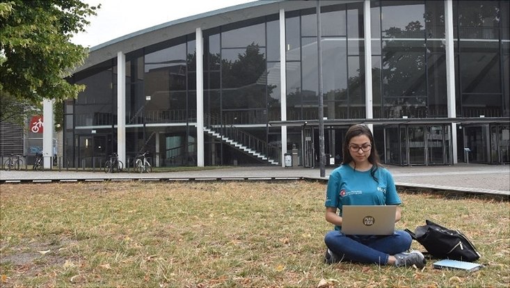 Studentin mit Laptop auf einer Rasenfläche sitzend auf dem Campusgelände