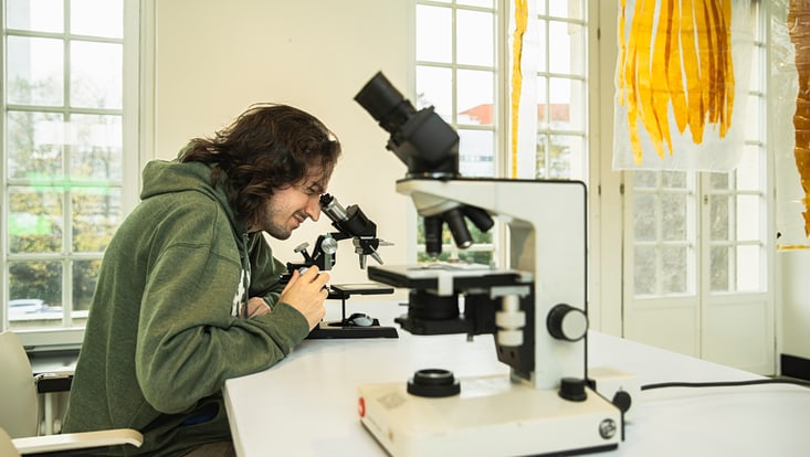 Mann mit dunklen Haaren beugt sich über ein Mikroskop
