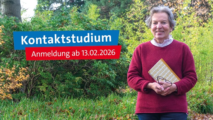 Lächelnde Frau um die 70 Jahre mit grauen, kurzen Haaren und rotem Pullover, die im Grünen stehen mit einem Buch und einer Brille in der Hand