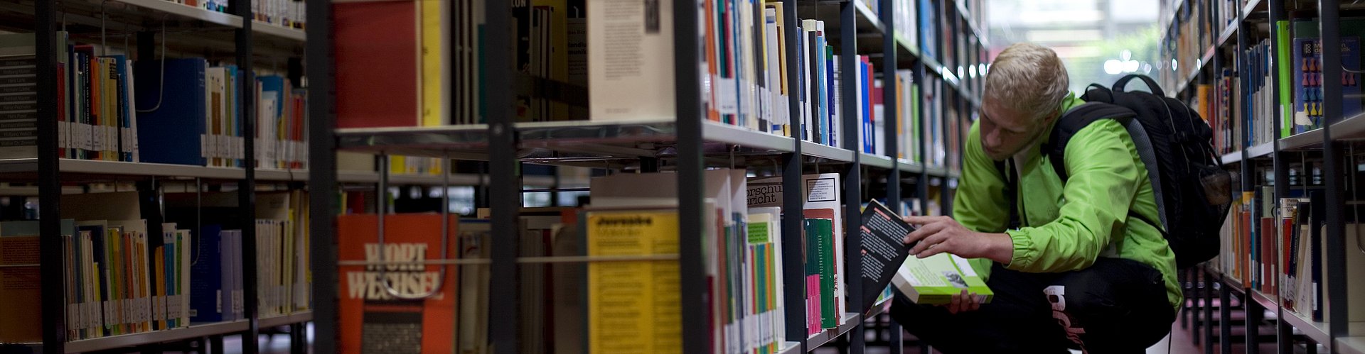 Ein Student sucht ein Buch in einem Bücherregal der Hochschulbibliothek