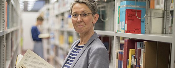Eine Person steht zwischen Bücherregalen in einer Bibliothek.