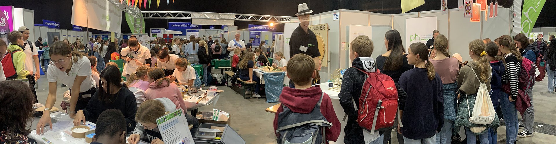 Stand der Pädagogischen Hochschule Karlsruhe bei den Science Days: Links vollbesetzte Tische mit bastelnden Kindern, rechts stehnde Kinder von hinten, die alles neugierig ansehen.