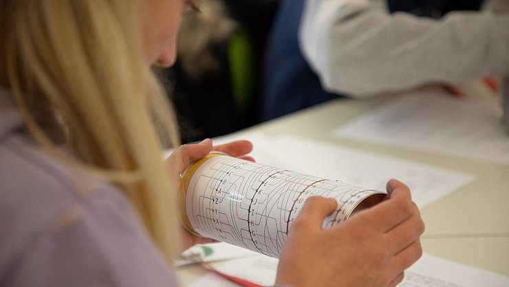 Eien Schülerin von hinten, die konzentriert auf bildlich dargestellte Programmierschritte auf einer Rolle blickt.