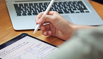 Eine Person, von hinten fotografiert, arbeitet mit Touch Pen und Laptop.